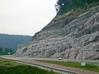 The basal half of this photograph of the road cut is of the Lower Mississippian Newman Limestone. This is composed of relatively continuous beds of shallow water carbonate that locally develop mounds and are channeled. Beds have irregular but sharp bedding planes and some shale partings and siltstones. At the top of the outcrop are the clastic rich Mississippian Upper Newman and Pennington Formations