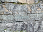 A change in base level is interpreted to have been responsible for the more prominent bedding planes, though storm waves are believed to have eroded across this shelf and caused these shallow water limestones of the Lower Mississippian Newman Limestone Formation to have their locally irregular character; while local currents accounted for the development of low angle cross beds (see center of photograph) and mound margin clinoforms suggesting migrating carbonate bodies moving across this setting. Note shale beds and filled bedding plane partings. Unit 94 from base to green layer, see the measured Geological Section, Kentucky Geological Survey Field Trip Guide 1998